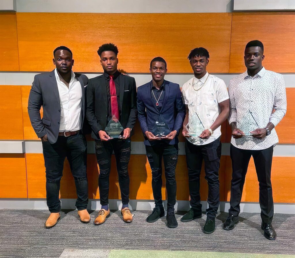 Men's Soccer players with Head Coach Oniqueky Samuels, showing off some awards.