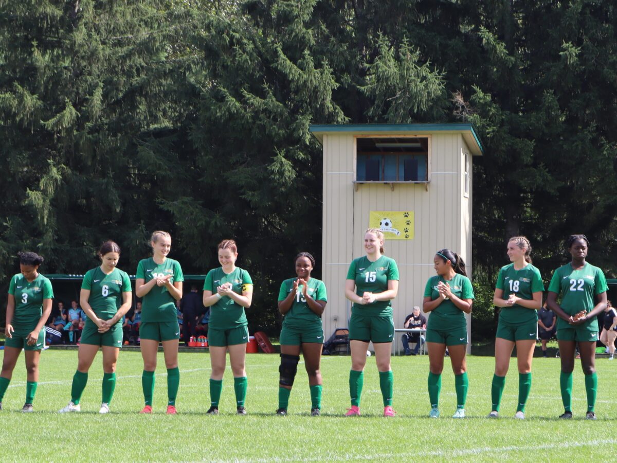 women's soccer team starting lineup stand together on the soccer field