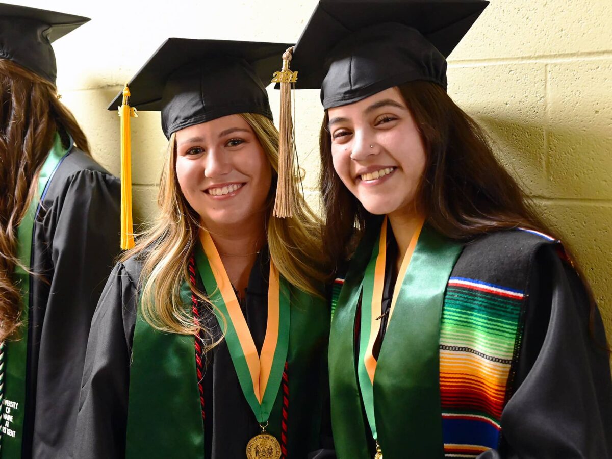 two female UMFK graduates smile for the camera as they wait for the 2024 commencement ceremony to start