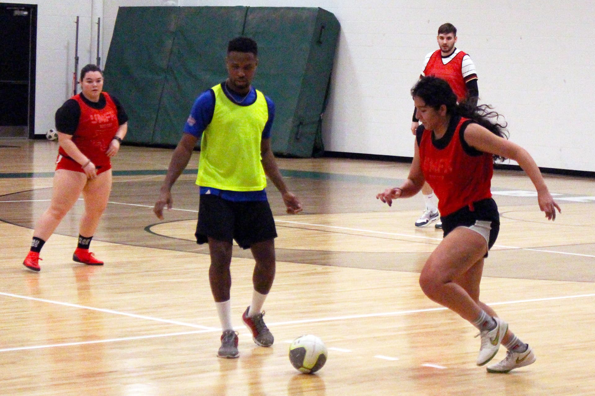 A group of UMFK students play indoor soccer, with each team wearing different colored jerseys