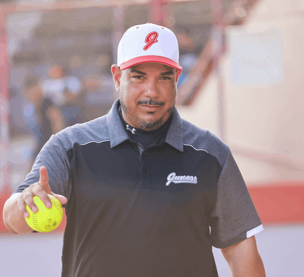 softball coach Luis Pérez in baseball cap holding a softball in his right hand