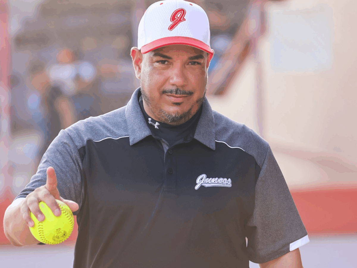 softball coach Luis Pérez in baseball cap holding a softball in his right hand